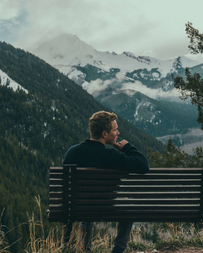 A man sits on a bench overlooking mountains