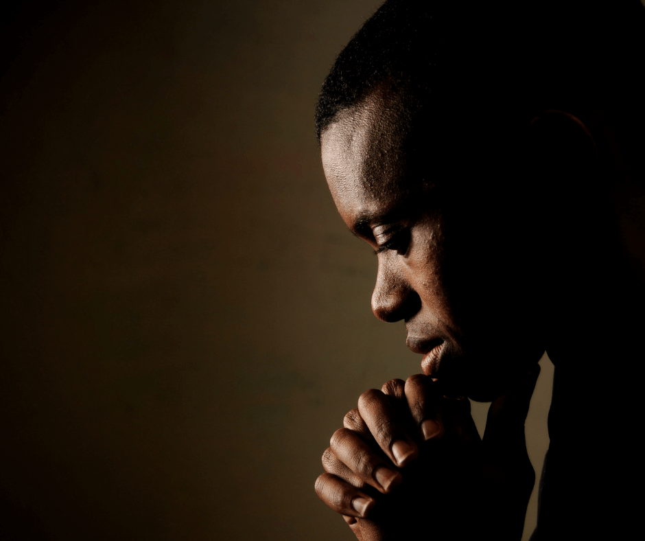 A black man sits in prayer