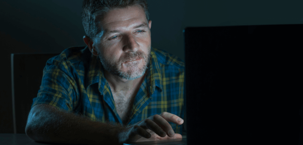 young aroused and excited sex addict man watching porn mobile online in laptop computer light night at home desk in pornography addiction and internet pornographic content concept