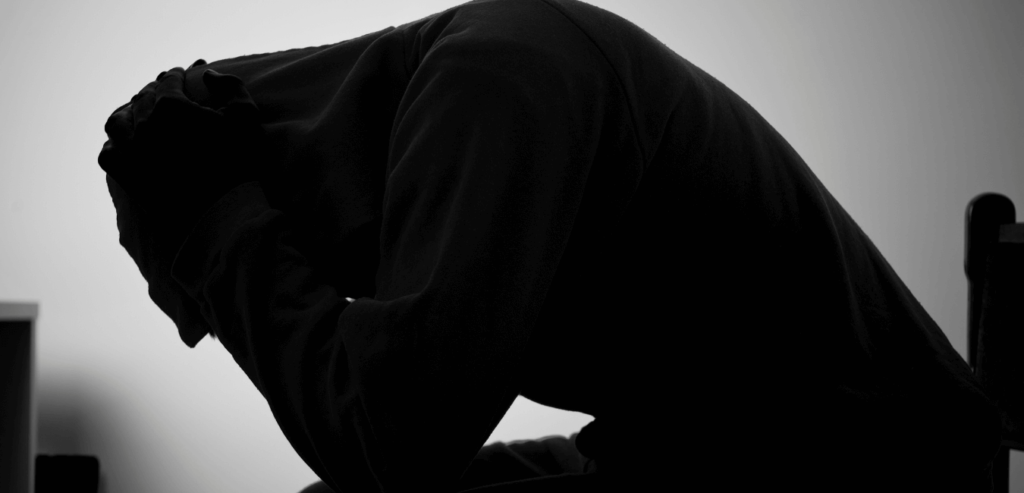 A silhouette of a man sitting on a chair with with his head down in a depressed state